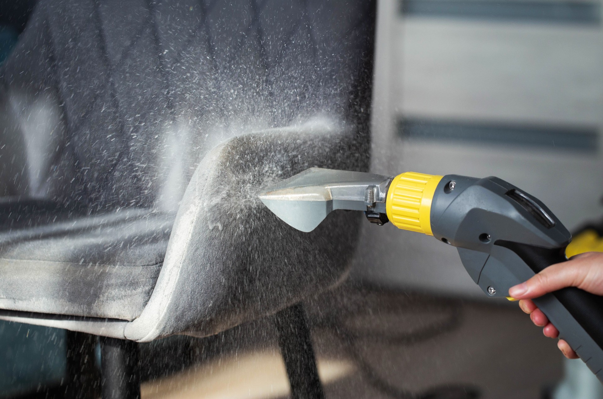 Spraying a chemical from a washing vacuum cleaner when cleaning the fabric upholstery of a chair. Cleaning services, industry